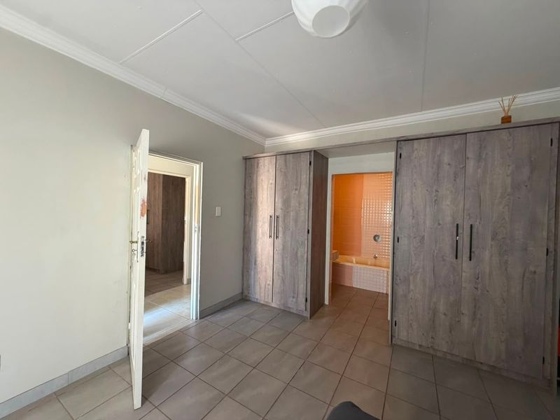 A spacious bedroom featuring tiled flooring, built-in cupboards, and direct access to an en-suite bathroom.