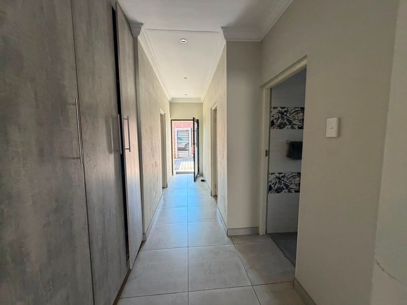 A bright, modern hallway featuring neutral tiled flooring, recessed downlighting, and extensive built-in storage cupboards.