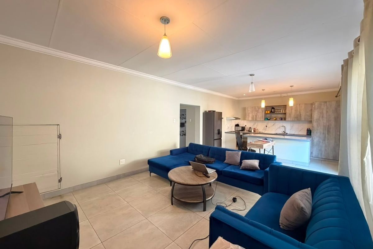 Open-plan living area featuring a modern kitchen with island, tiled flooring, and neutral wall finishes, creating a spacious and functional layout.