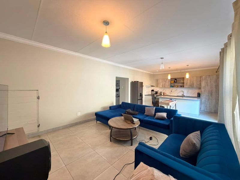 Open-plan living area featuring a modern kitchen with island, tiled flooring, and neutral wall finishes, creating a spacious and functional layout.
