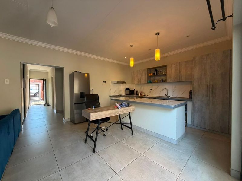 Open-plan kitchen featuring modern cabinetry, a central island, and tiled flooring, seamlessly connecting to the main living area and hallway.