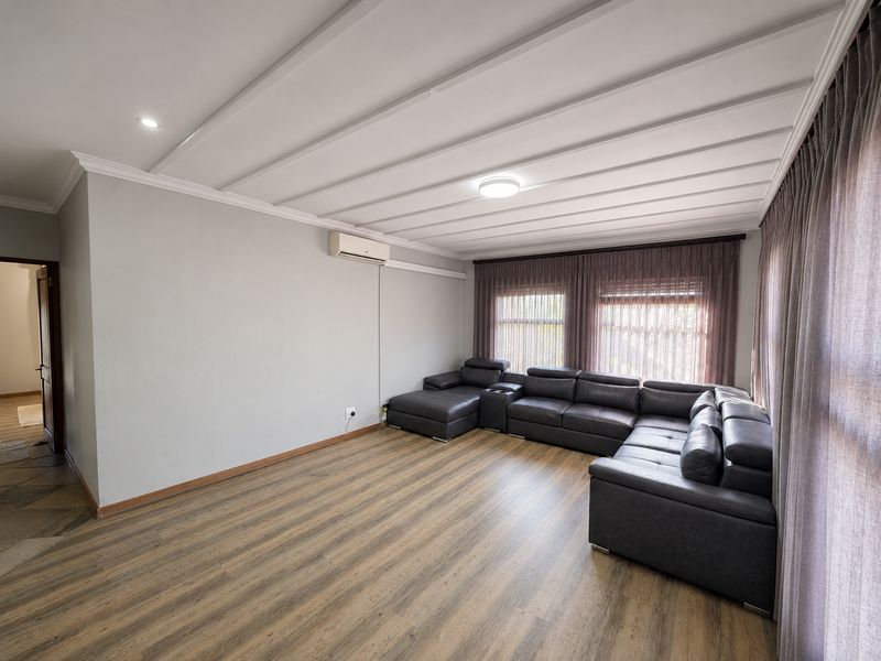 Spacious living room featuring wood-look laminate flooring, a wall-mounted air conditioning unit, and distinctive panelled ceiling detail.
