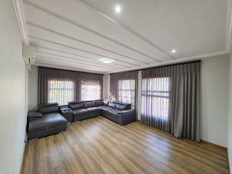 A spacious living room featuring wood-look laminate flooring, recessed downlighting, and a wall-mounted split-system air conditioner, complemented by floor-to-ceiling window treatments.