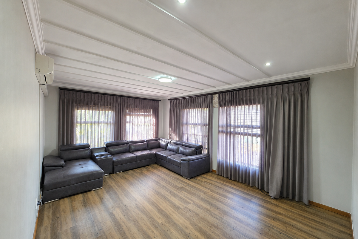 A spacious living room featuring wood-look laminate flooring, recessed downlighting, and a wall-mounted split-system air conditioner, complemented by floor-to-ceiling window treatments.