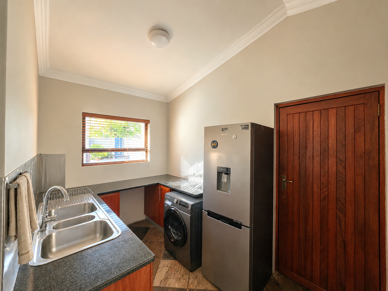 A functional laundry room featuring a double stainless steel sink, laminate countertops, wooden cabinetry, and a solid timber door.