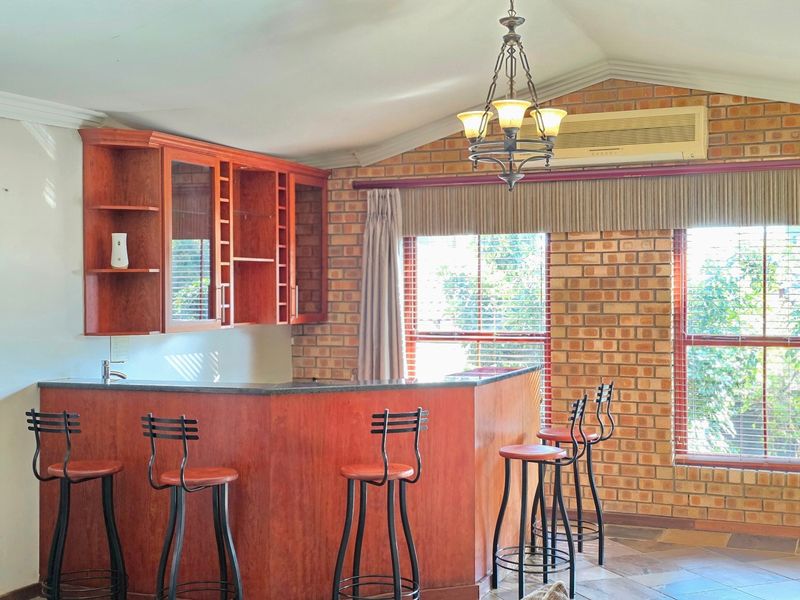 A rustic bar area featuring exposed brick walls, a vaulted ceiling, built-in wooden cabinetry, and a stone-topped bar counter.