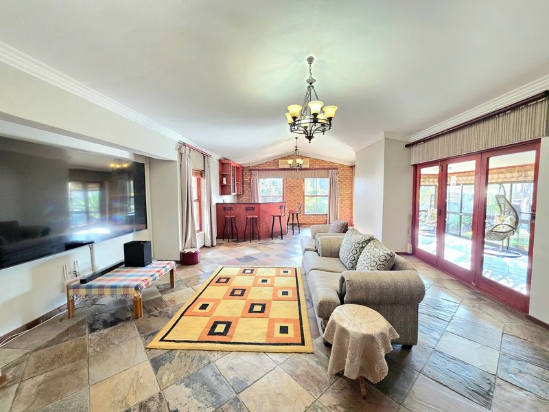 Spacious open-plan living area featuring stone tile flooring, a built-in bar, exposed brick accents, vaulted ceilings, and direct access to the patio.