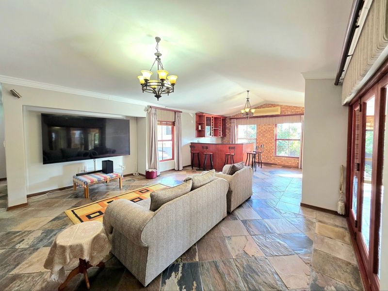 Spacious open-plan living area featuring stone tile flooring, a built-in bar, exposed brick accents, and vaulted ceilings with direct access to the patio.
