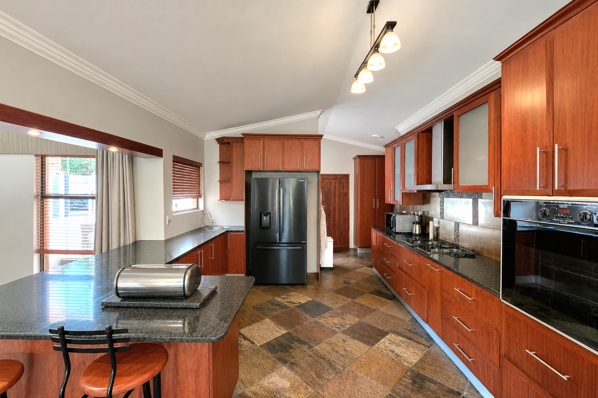 Spacious kitchen featuring cherry wood cabinetry, granite countertops, built-in oven, gas hob, and durable slate tile flooring with a breakfast bar area.