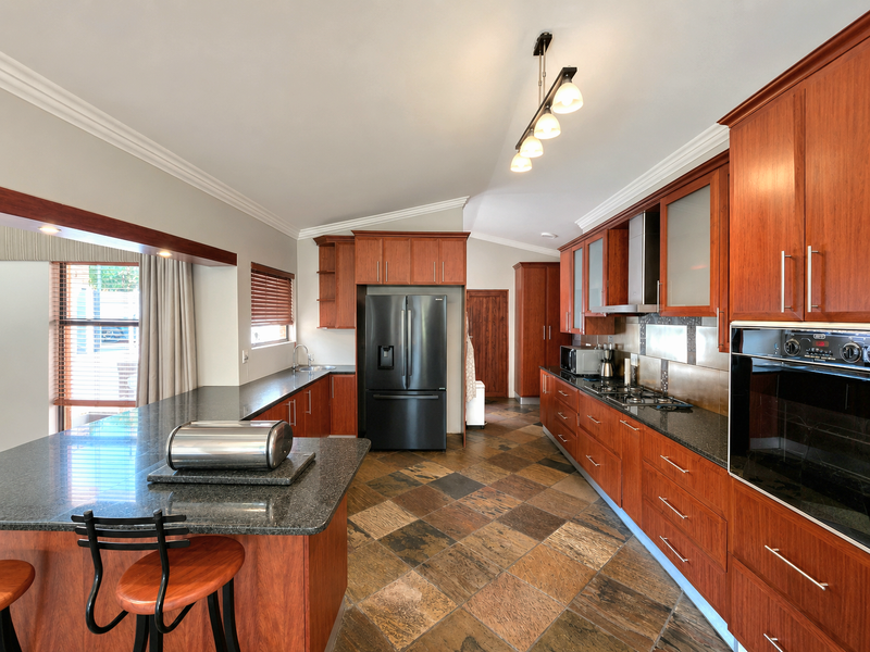 Spacious kitchen featuring cherry wood cabinetry, granite countertops, built-in oven, gas hob, and durable slate tile flooring with a breakfast bar area.