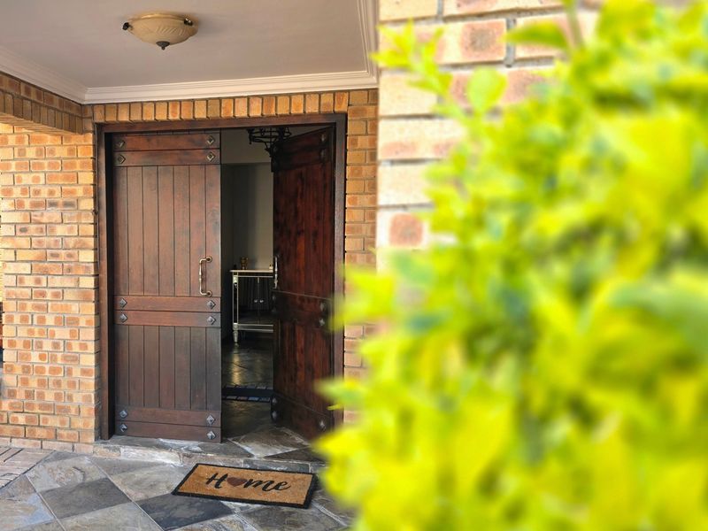 A welcoming entrance featuring rustic double timber doors, exposed brickwork, and durable stone tile flooring under a covered porch area.