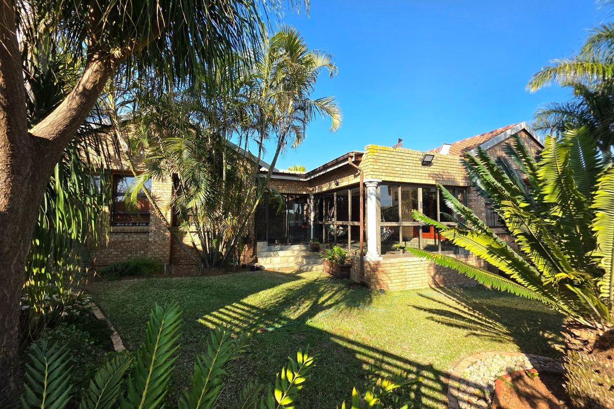 Rear view of the house featuring a brick facade, an enclosed patio area, and a well-established garden with mature trees.