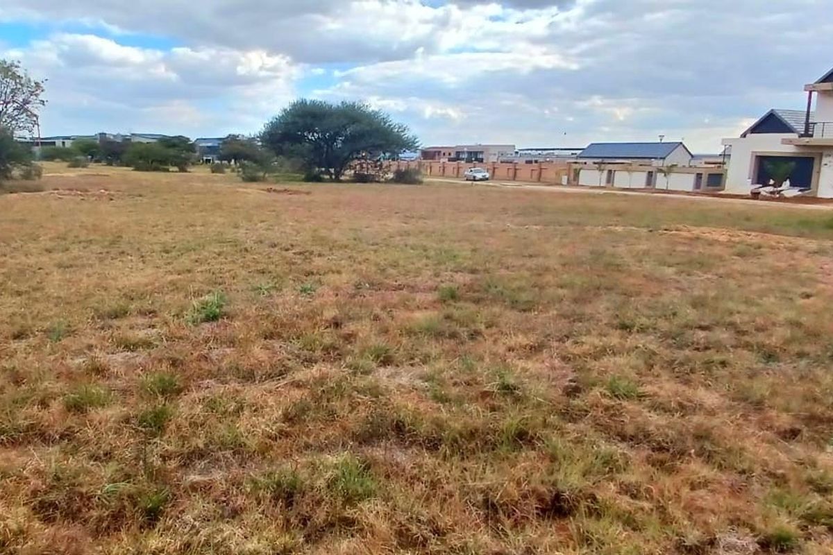 A view of a vacant residential plot of land with surrounding neighborhood development visible in the background.