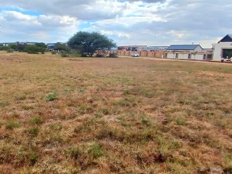 A view of a vacant residential plot of land with surrounding neighborhood development visible in the background.