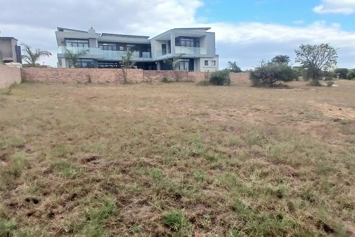 A view of a vacant residential plot featuring a boundary wall with established neighboring properties in the background.