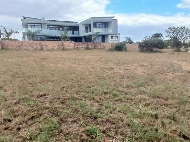 A view of a vacant residential plot featuring a boundary wall with established neighboring properties in the background.