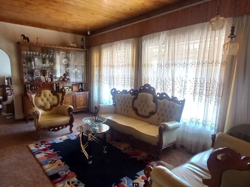 A traditional living room featuring a warm timber-clad ceiling, an arched entryway, and large windows that allow for natural light.