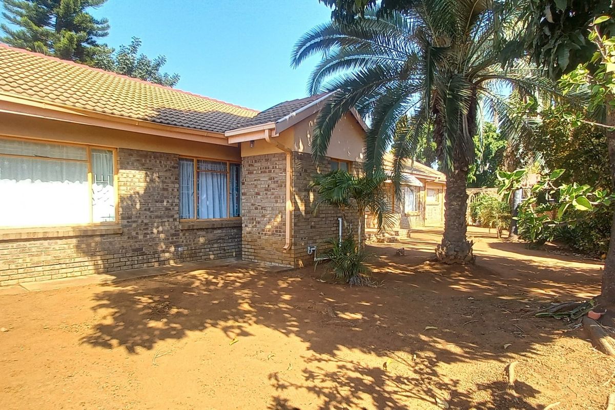 Rear view of a face brick house with a tiled roof, featuring security bars on windows and an unpaved garden area.
