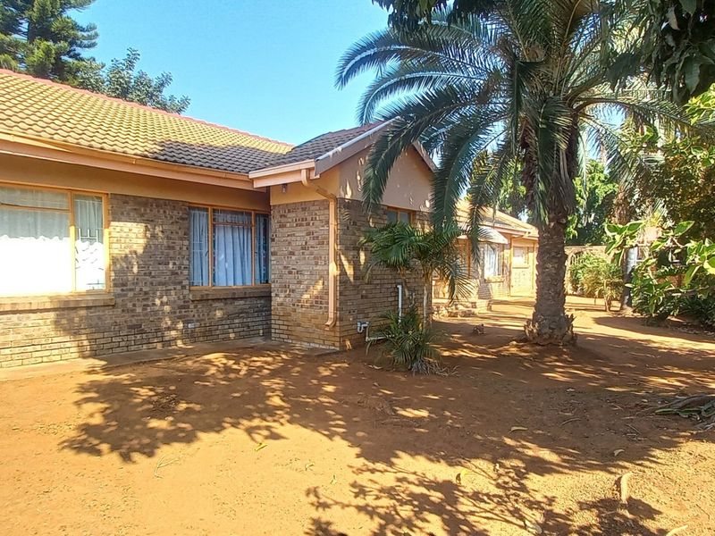 Rear view of a face brick house with a tiled roof, featuring security bars on windows and an unpaved garden area.