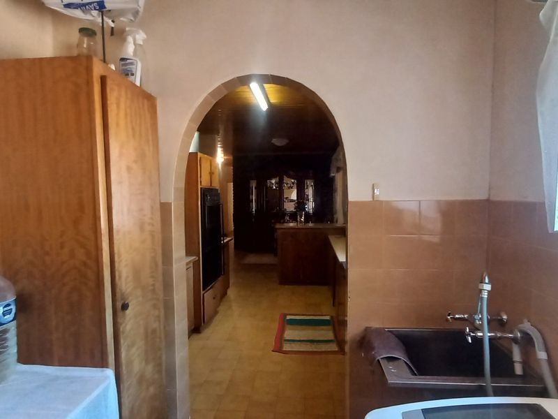 A functional laundry area featuring built-in cabinetry, a utility sink, and tiled splashbacks, leading through an archway into the adjacent living space.