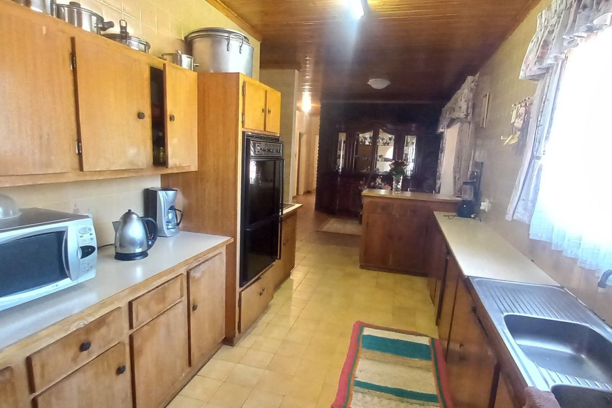 A dated kitchen featuring wooden cabinetry, integrated oven, stainless steel sink, and timber ceiling, offering significant potential for a modern renovation.