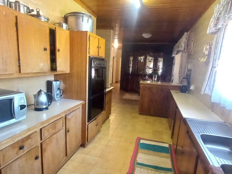 A dated kitchen featuring wooden cabinetry, integrated oven, stainless steel sink, and timber ceiling, offering significant potential for a modern renovation.