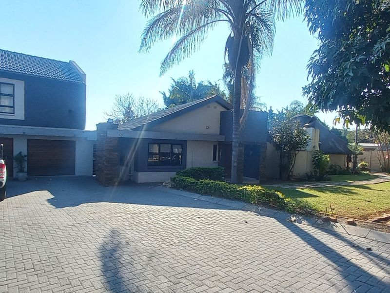 Front exterior view of a well-maintained house featuring a paved driveway, double garage, and established garden area.