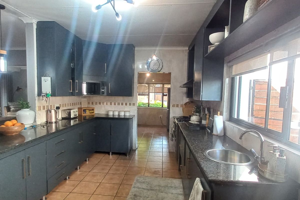 A functional kitchen featuring dark cabinetry, granite countertops, tiled flooring, and a tiled backsplash, with an open-plan layout connecting to the living area.