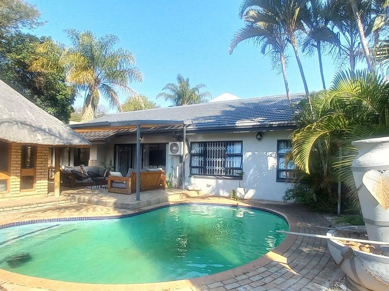 Outdoor pool area featuring a swimming pool, brick paving, a covered patio, and a thatched roof structure.