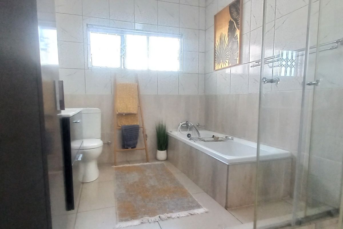 A well-maintained bathroom featuring a bathtub, a separate glass-enclosed shower, and neutral wall and floor tiling.