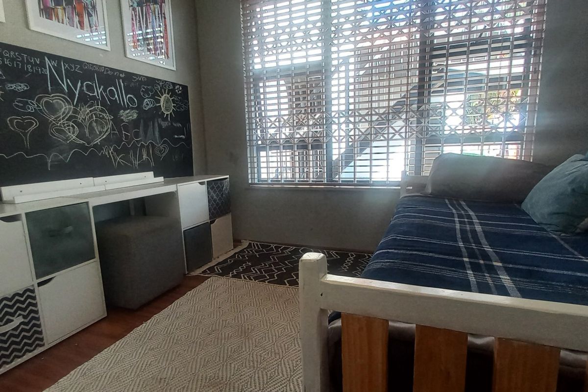A bedroom featuring laminate flooring, a built-in chalkboard wall, and a window fitted with security gates and venetian blinds.