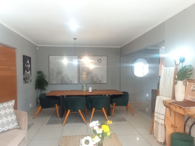 An open-plan living and dining area featuring neutral grey walls, tiled flooring, and modern lighting fixtures, creating a cohesive and inviting space.