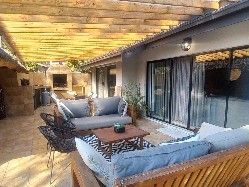 Spacious covered patio featuring a timber pergola, built-in braai, and tiled flooring, providing a seamless transition between indoor and outdoor living areas.