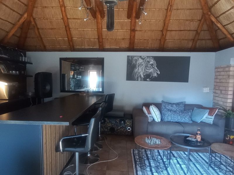 A rustic bar area featuring a traditional thatched roof with exposed timber rafters, a built-in bar counter, and tiled flooring.