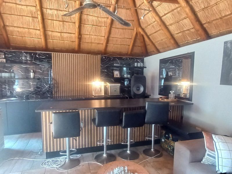 A rustic bar area featuring a high thatched ceiling, ceiling fan, and a modern built-in bar counter with stylish slatted timber and marble-effect finishes.