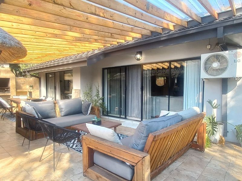 Covered outdoor patio featuring a timber pergola, tiled flooring, and a built-in braai area, providing a functional space for outdoor entertaining.