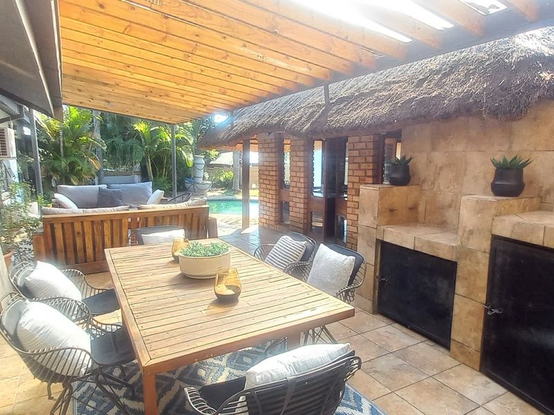 Covered outdoor patio featuring a built-in braai, thatched roof, and timber pergola, providing a functional space for alfresco dining and entertainment.