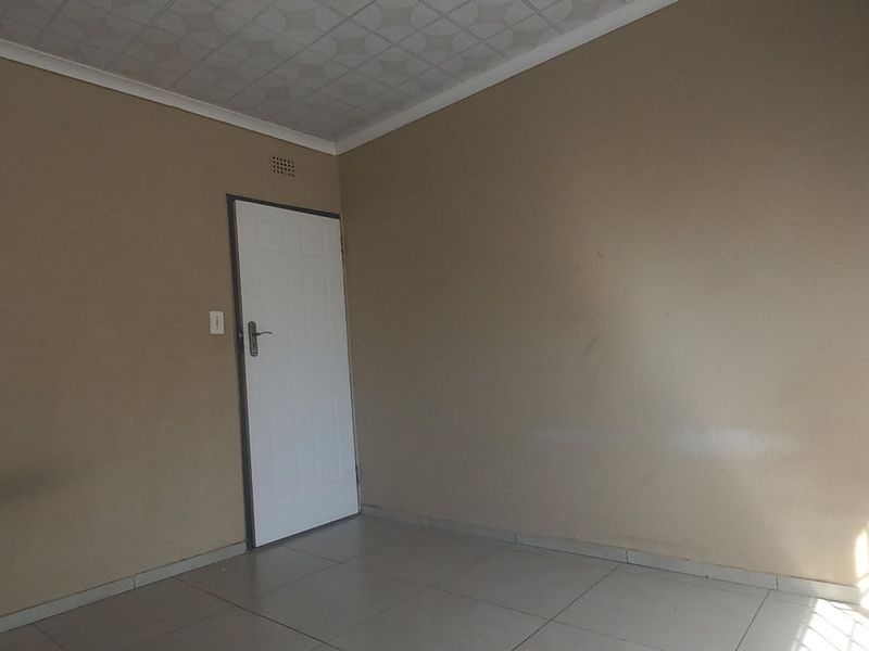 An empty bedroom featuring tiled flooring, a standard internal door, and patterned ceiling tiles, offering a blank canvas for potential interior updates.