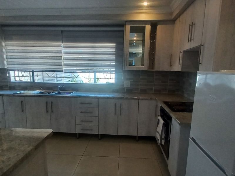 Modern kitchen featuring light-toned cabinetry, stone countertops, a tiled backsplash, and integrated appliances, offering a clean and functional workspace.