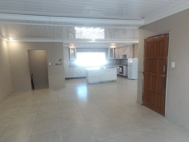 Spacious open-plan living and kitchen area featuring tiled flooring, a central kitchen island, and a paneled ceiling.