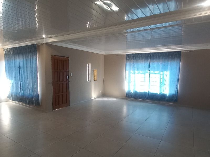 Spacious, open-plan living area featuring neutral tiled flooring, modern PVC ceiling panels with recessed lighting, and multiple access points.