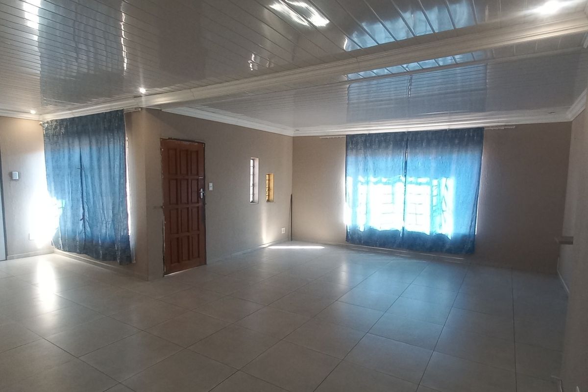 Spacious, open-plan living area featuring neutral tiled flooring, modern PVC ceiling panels with recessed lighting, and multiple access points.