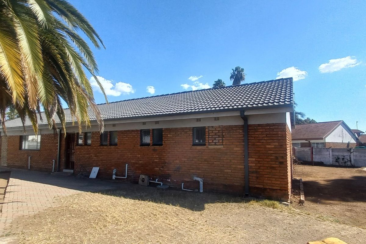 Rear view of a single-story brick house featuring a tiled roof, paved walkway, and exposed exterior plumbing.