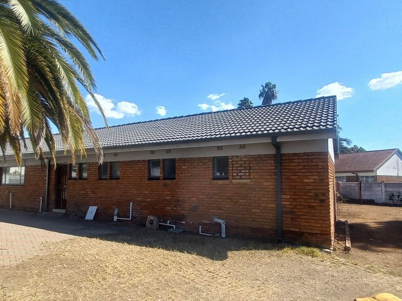Rear view of a single-story brick house featuring a tiled roof, paved walkway, and exposed exterior plumbing.