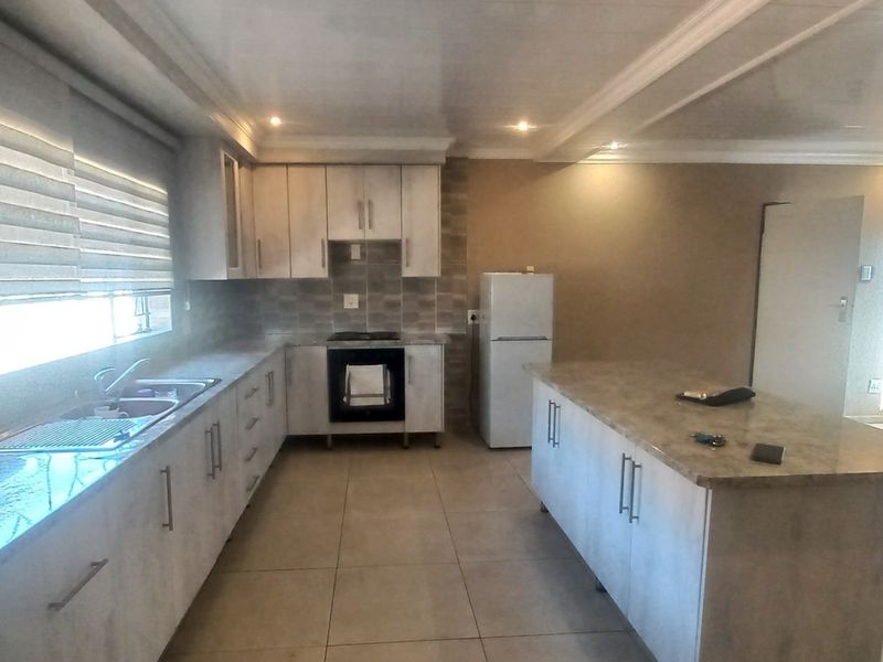 Modern kitchen featuring light-toned cabinetry, stone countertops, a central island, and integrated appliances with tiled flooring and recessed lighting.