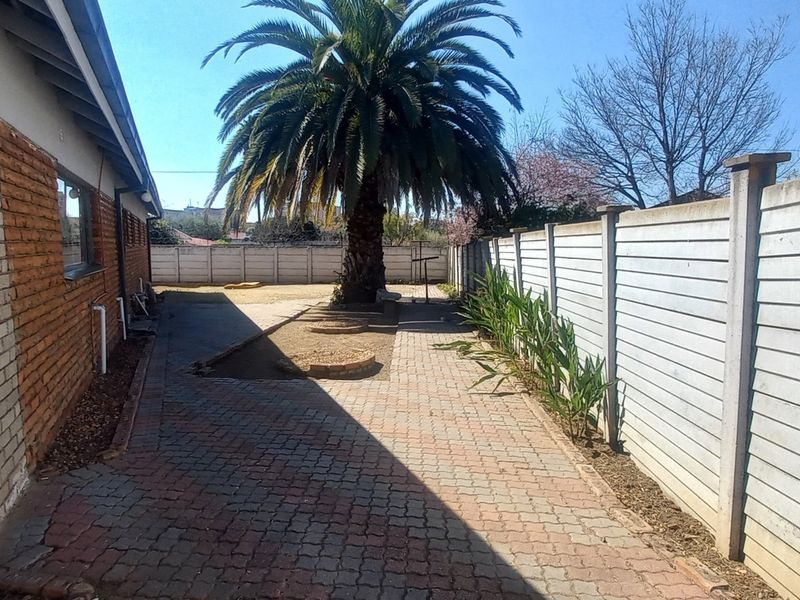 A rear exterior view showing a brick-paved side yard, precast concrete boundary wall, and a large palm tree.