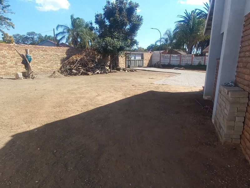 A spacious rear yard area featuring a brick boundary wall, paved driveway access, and significant potential for landscaping and outdoor development.
