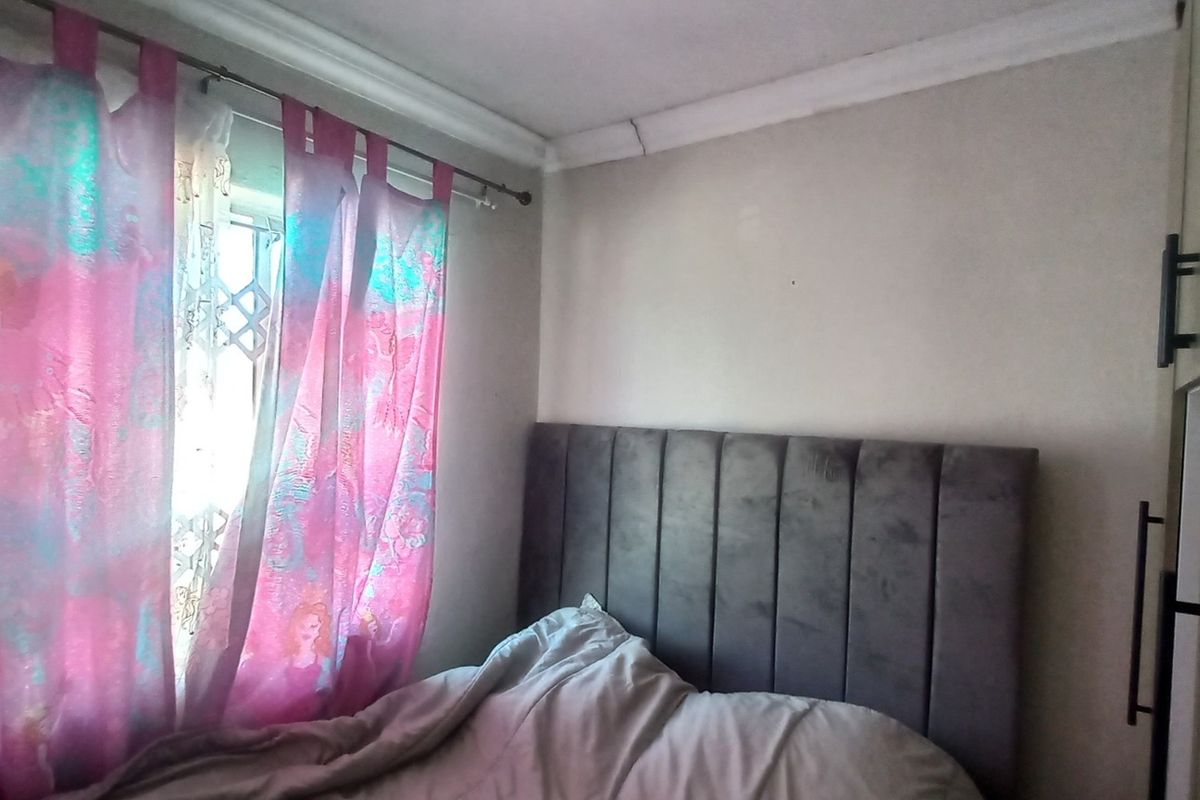 A bedroom featuring a built-in wardrobe and decorative ceiling cornice, with a security gate visible on the window.