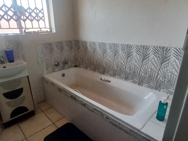 A functional bathroom featuring a built-in bathtub, vanity basin, and decorative tiled splashbacks, requiring some cosmetic updates to refresh the space.