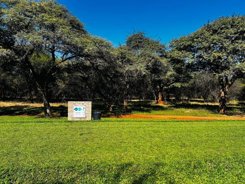 A view of a vacant residential plot featuring a well-maintained lawn, mature trees, and property signage.